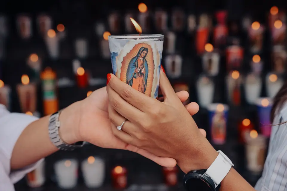 Las manos de ambos sostienen una veladora de la Virgen de Guadalupe