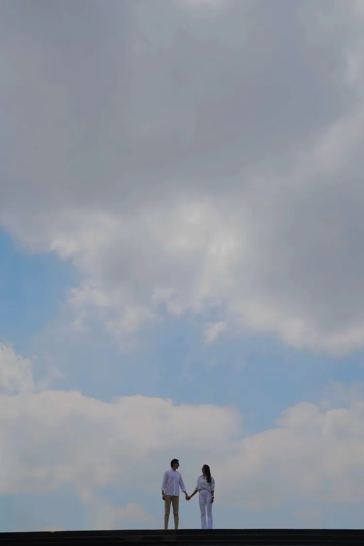 Andrea y Augusto tomados de la mano en lo alto de una escalinata, bajo un cielo enorme de nubes